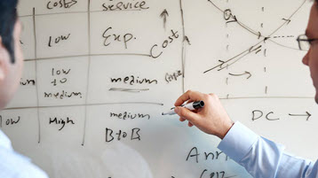Two men discussing supply chain consulting in front of a whiteboard