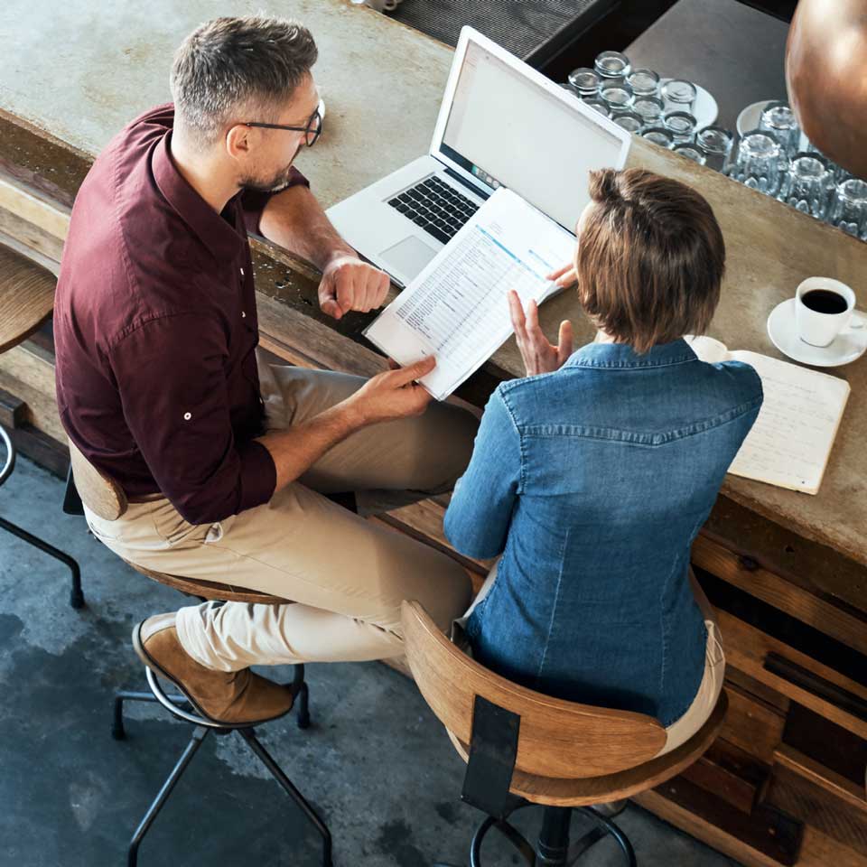 Aerial view of two people at a desk on a shared laptop 